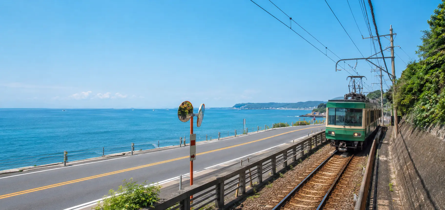 A green coastal train running beside a road and the sea near Kamakura.