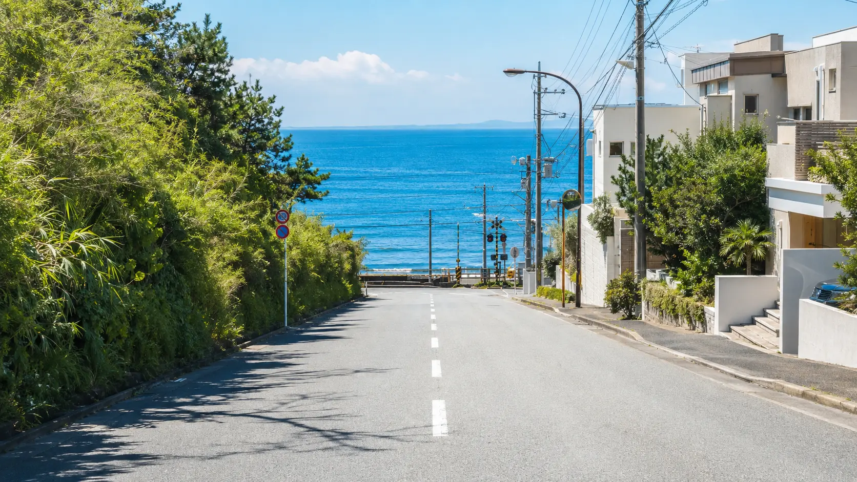 A sunlit residential road in coastal Kamakura descending toward the blue sea.